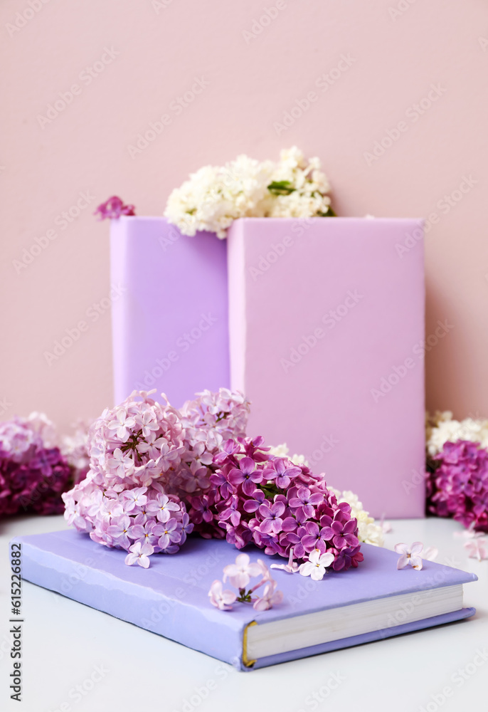 Beautiful fragrant lilac flowers with books on white table near pink wall