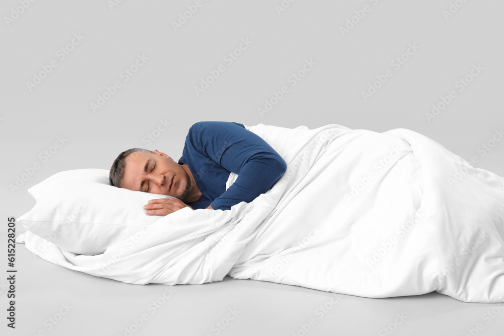 Mature man with soft blanket sleeping on grey background