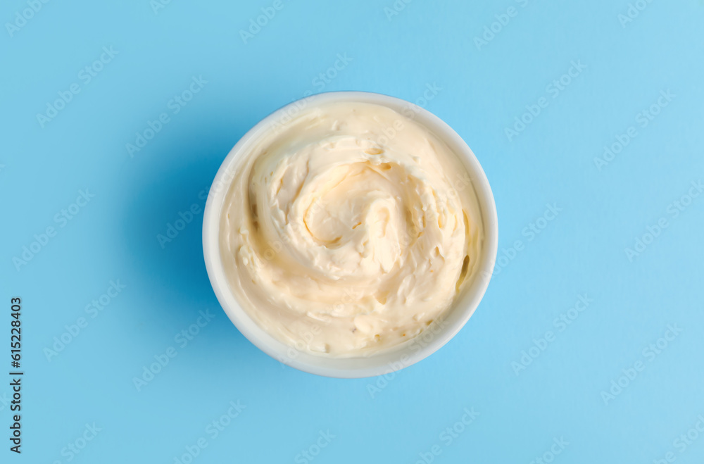 Bowl with tasty cream cheese on blue background