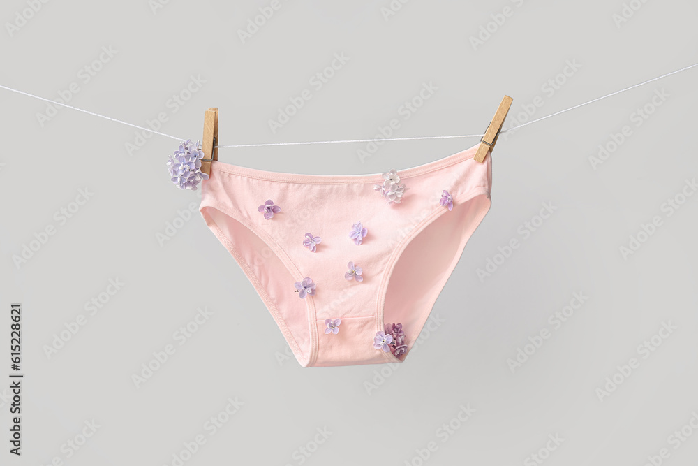 Stylish female panties with beautiful lilac flowers hanging on rope against white background