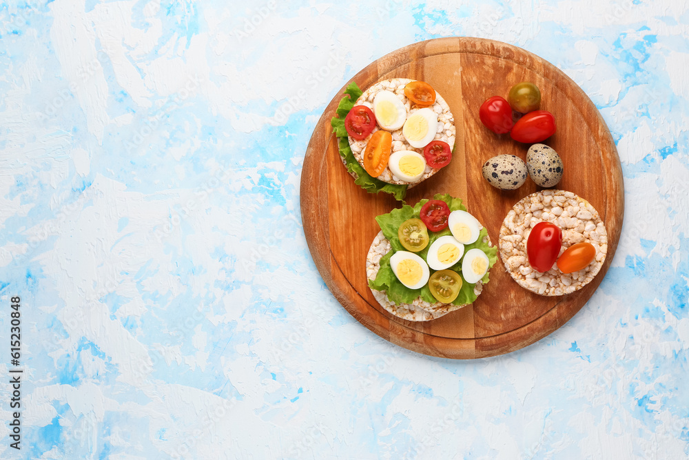 Rice crackers with quail eggs, tomatoes and lettuce on light blue background