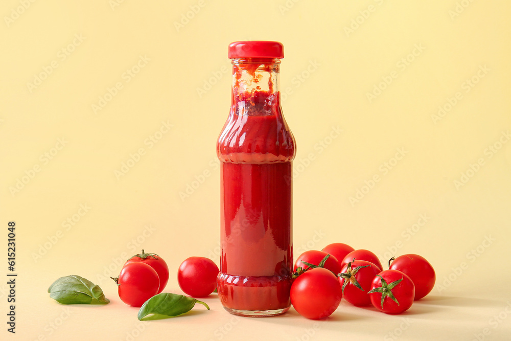 Glass bottle of ketchup and tomatoes on beige background