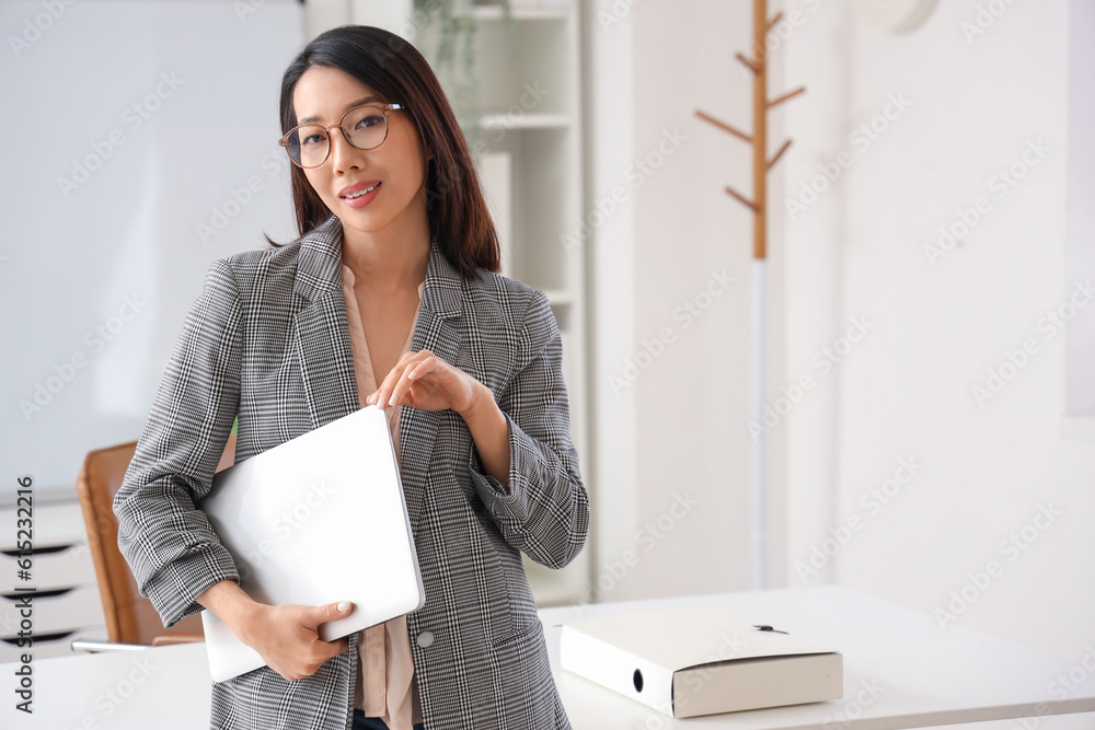 Beautiful Asian businesswoman in stylish eyeglasses with laptop in office