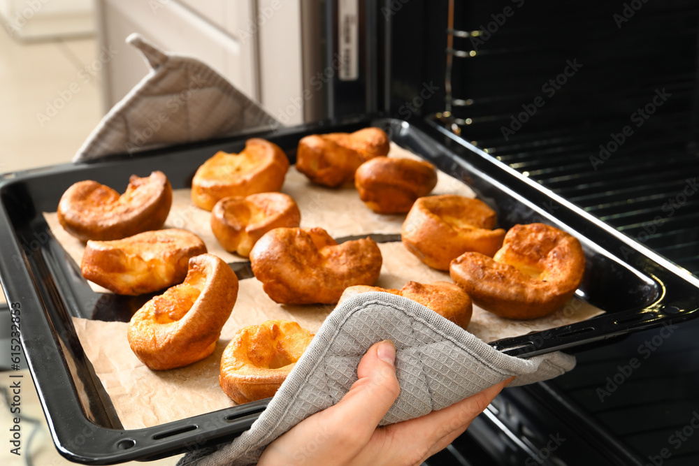 Woman taking baking tray with tasty Yorkshire pudding out from oven in kitchen