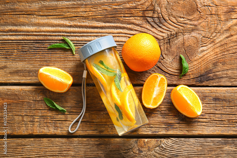 Sports bottle of infused water with orange slices on wooden background