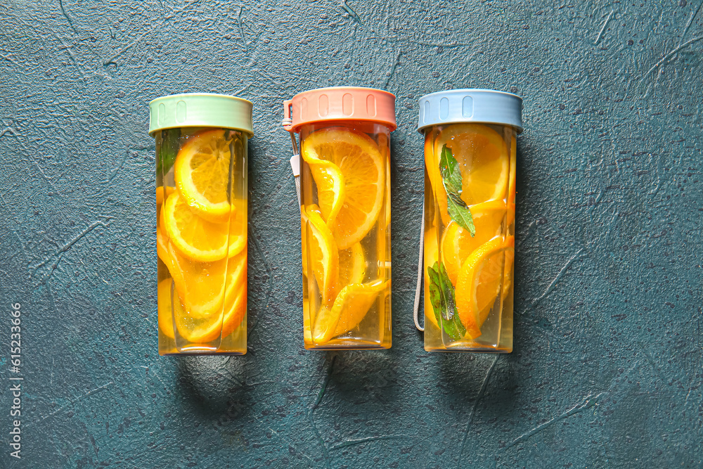 Sports bottles of infused water with orange slices on blue background