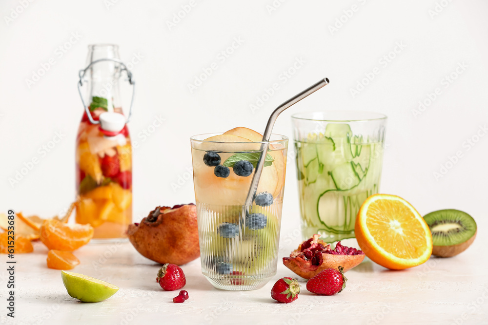 Glasses and bottle of infused water with different sliced fruits on white table