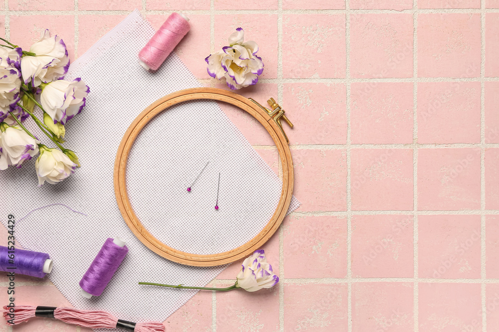 Embroidery hoop with canvas, threads and beautiful flowers on pink tile background