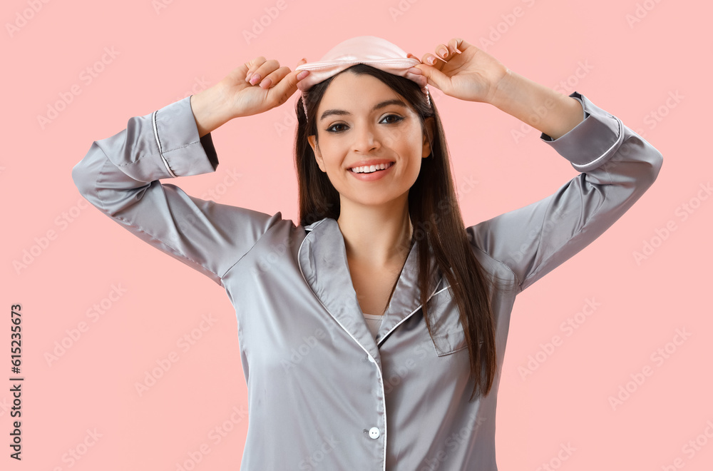 Young woman in pajamas with sleeping mask on pink background