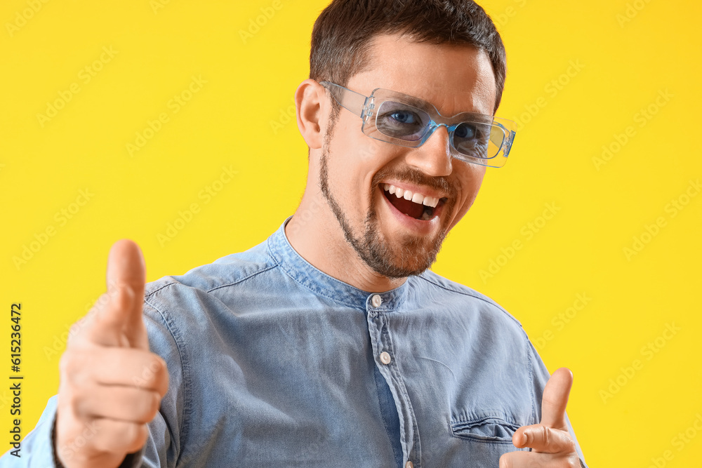 Handsome man in stylish sunglasses pointing at viewer on yellow background, closeup