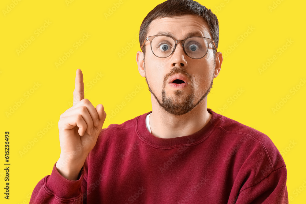 Handsome man in stylish eyeglasses having idea on yellow background, closeup