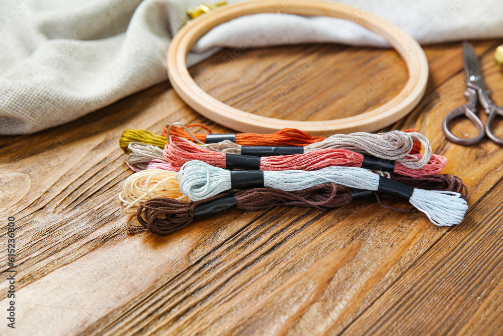 Embroidery hoop with mouline threads, scissors, thimble and canvas on brown wooden background