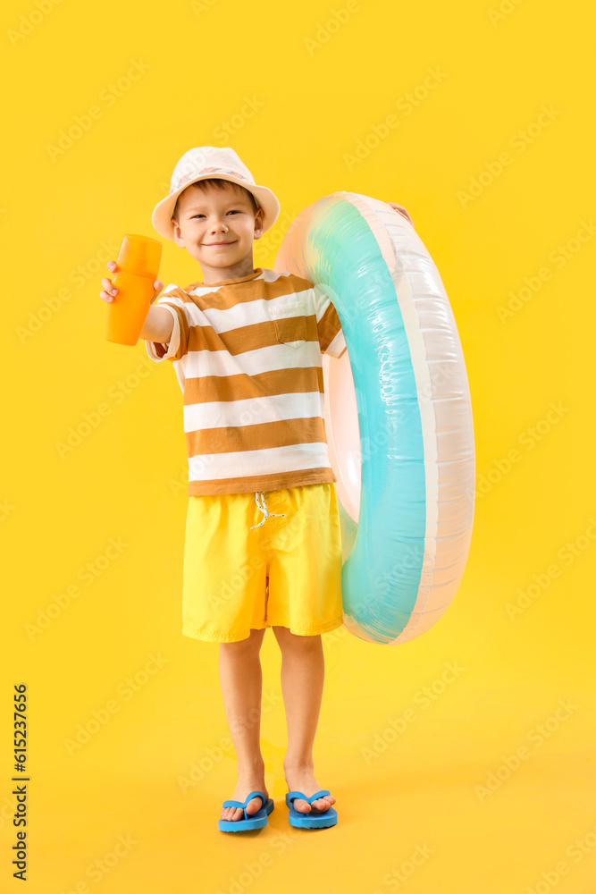 Little boy with bottle of sunscreen cream and inflatable ring on yellow background