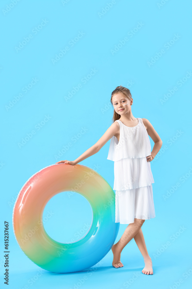 Little girl with inflatable ring and sunscreen cream on her face against blue background