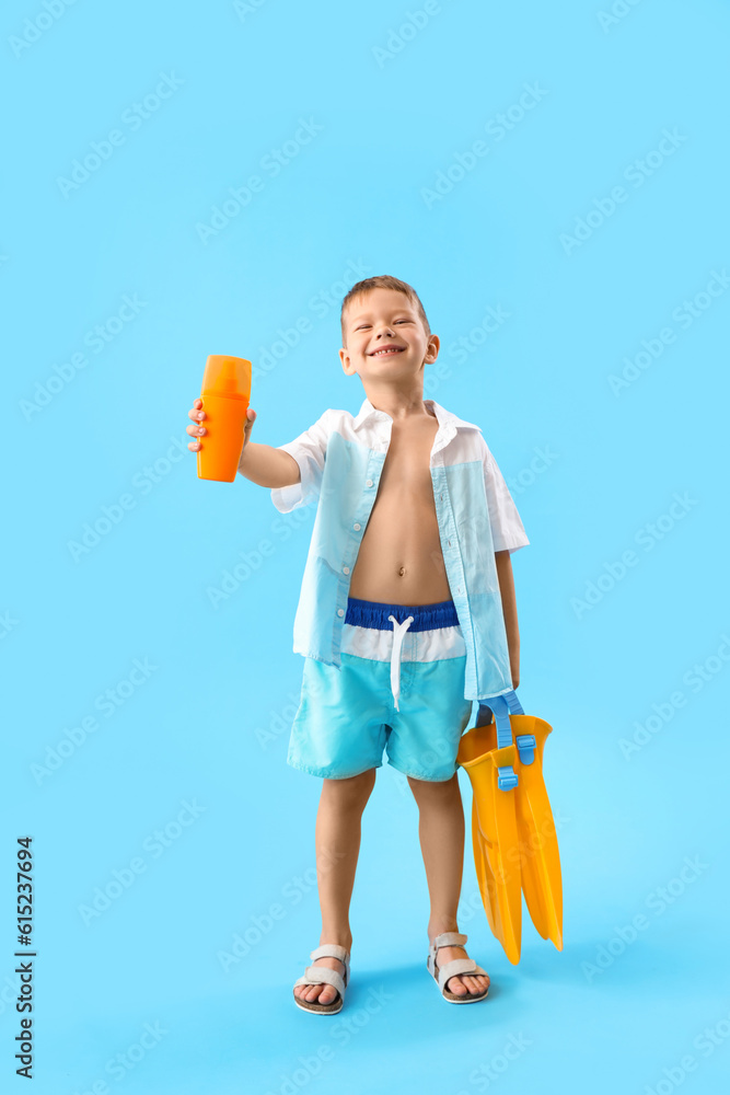 Little boy with bottle of sunscreen cream and flippers on blue background