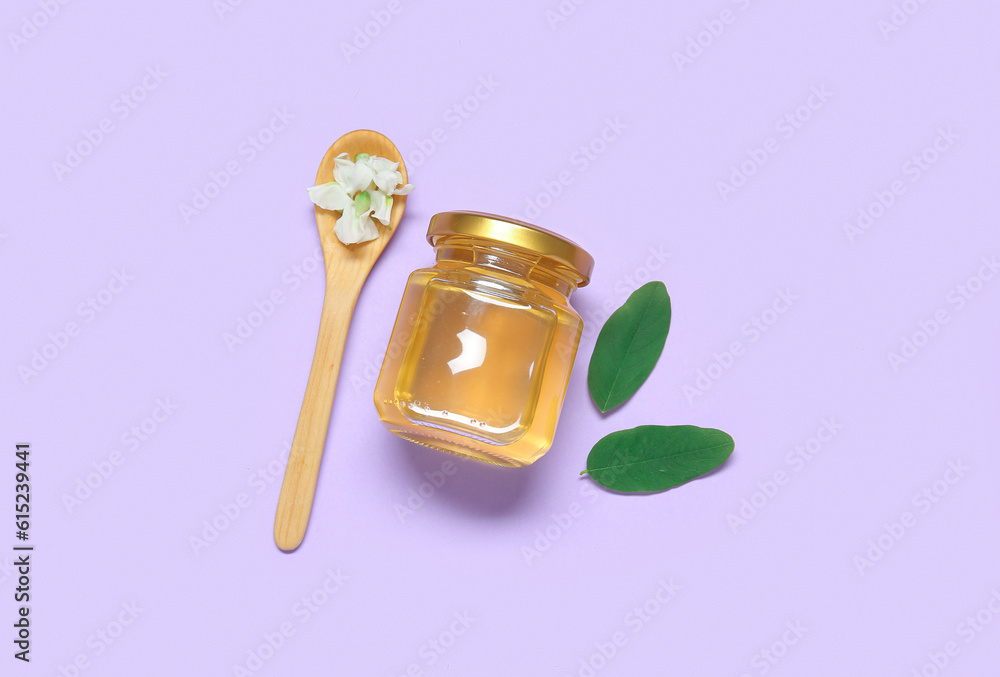 Jar of honey with flower of acacia and spoon on purple background