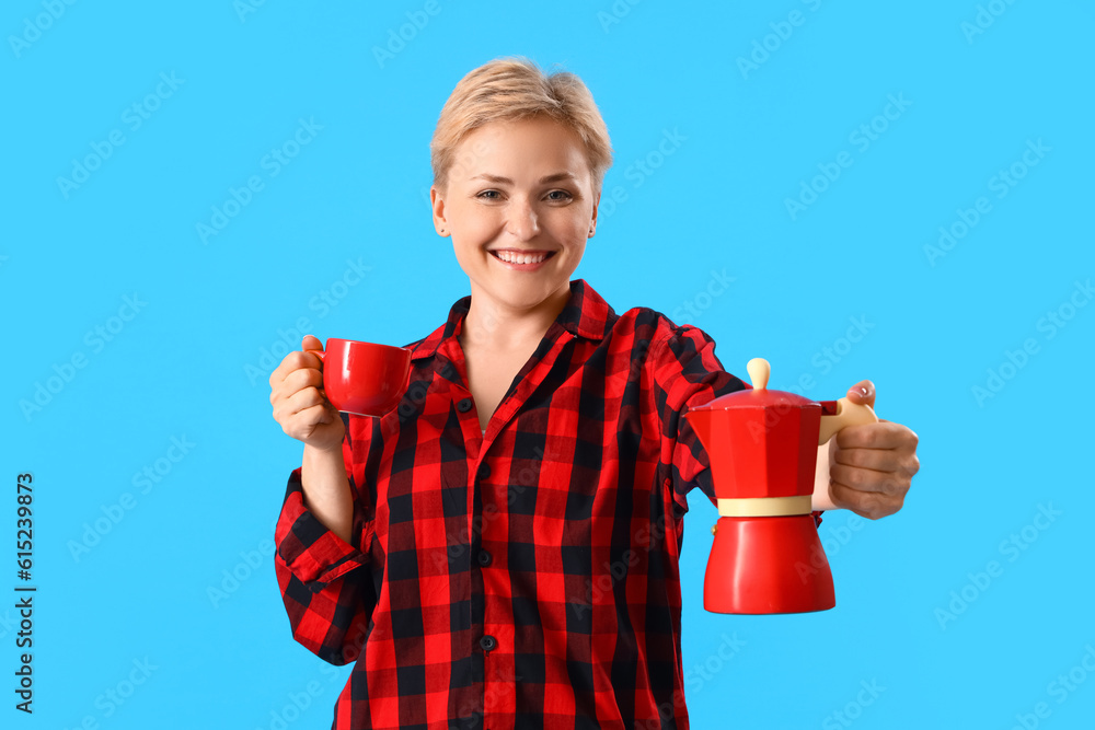 Young woman in pajamas with cup and coffee maker on blue background