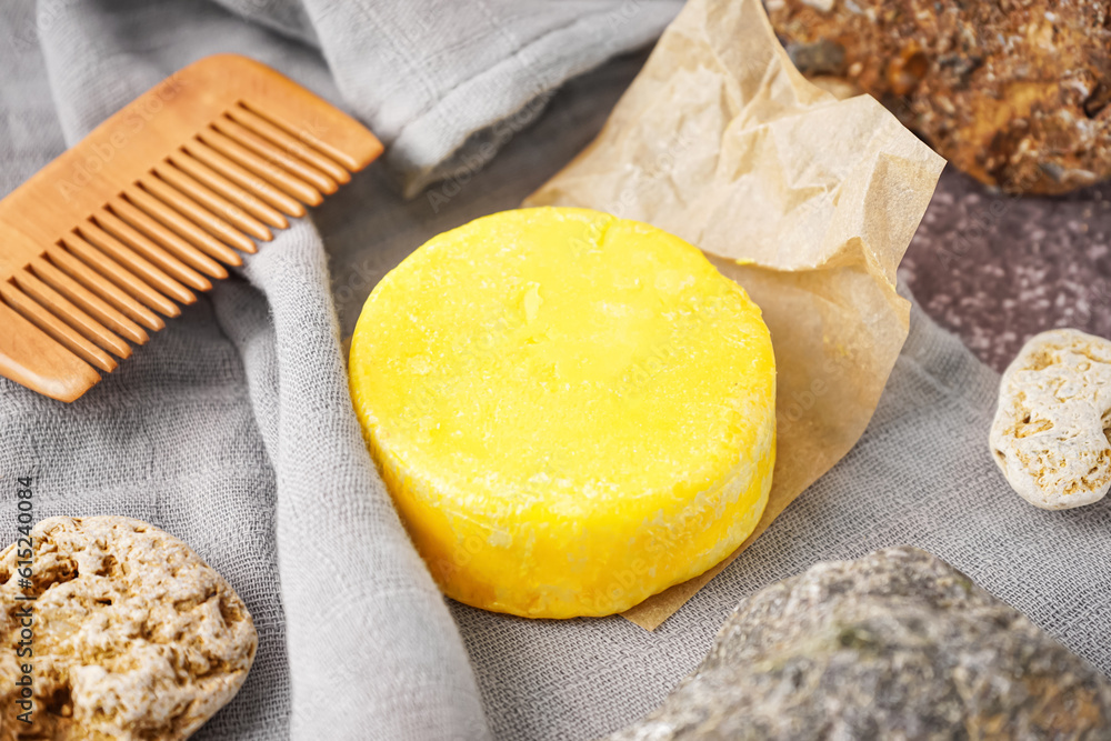 Yellow handmade solid shampoo, hair comb and stones on table, closeup