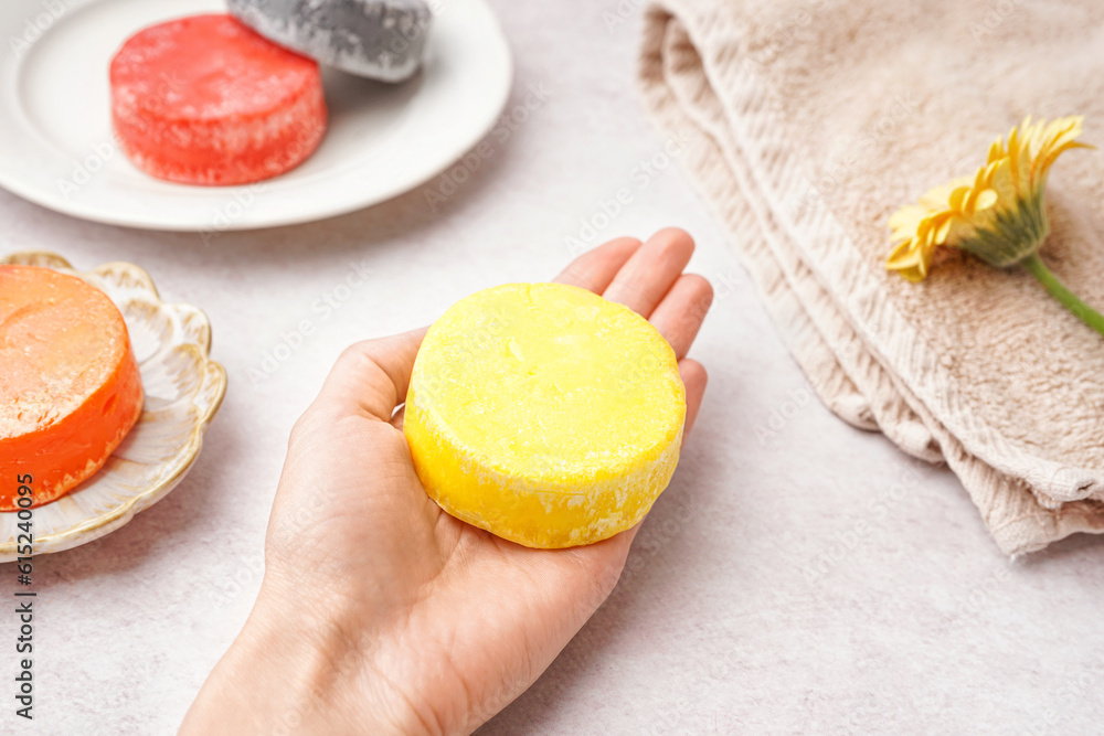 Female hand with handmade solid shampoo and calendula flower on light background, closeup