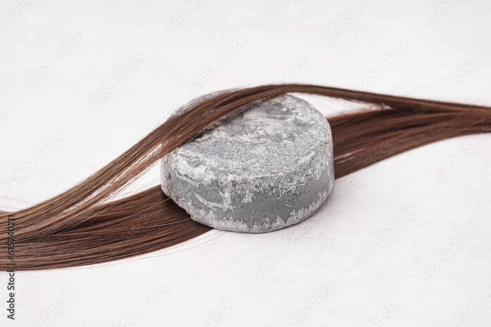 Handmade solid shampoo and brunette hair on light background, closeup