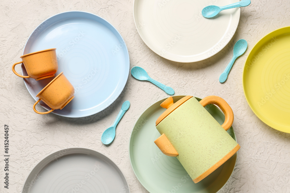 Plates with cups, teapot and spoons for baby on white background