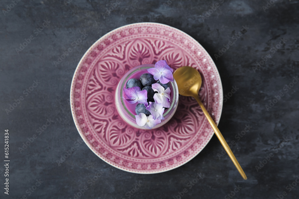 Glass of panna cotta with blueberry and beautiful hydrangea flowers on black table