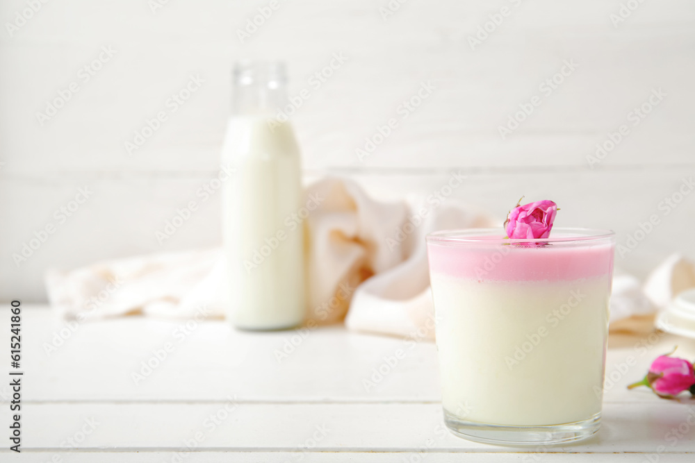 Glass of panna cotta with beautiful pink rose flowers on white wooden table