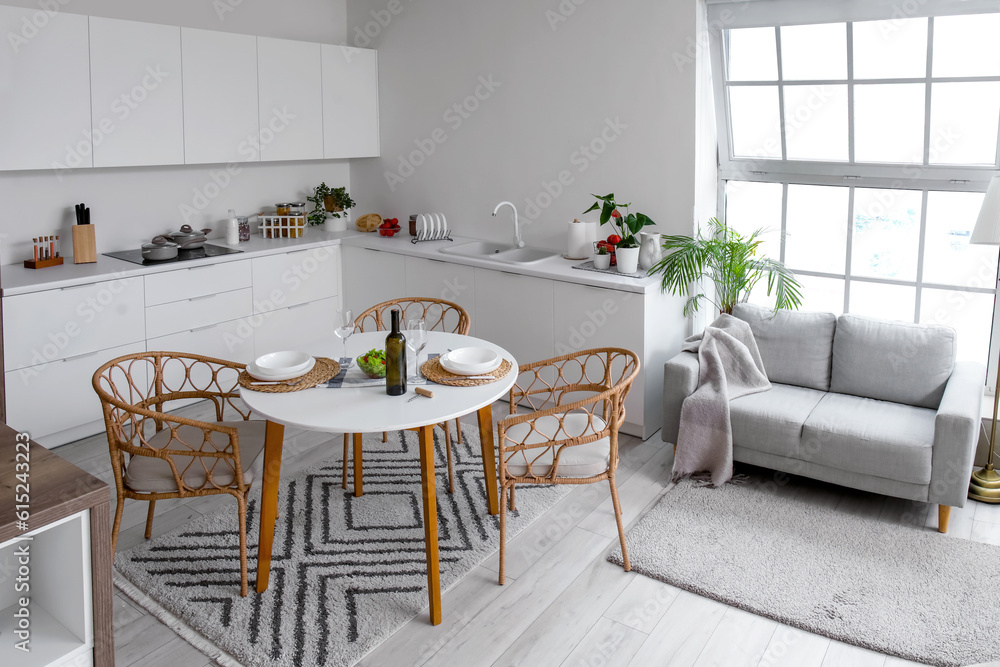 Interior of light open plan kitchen with served dining table and grey sofa