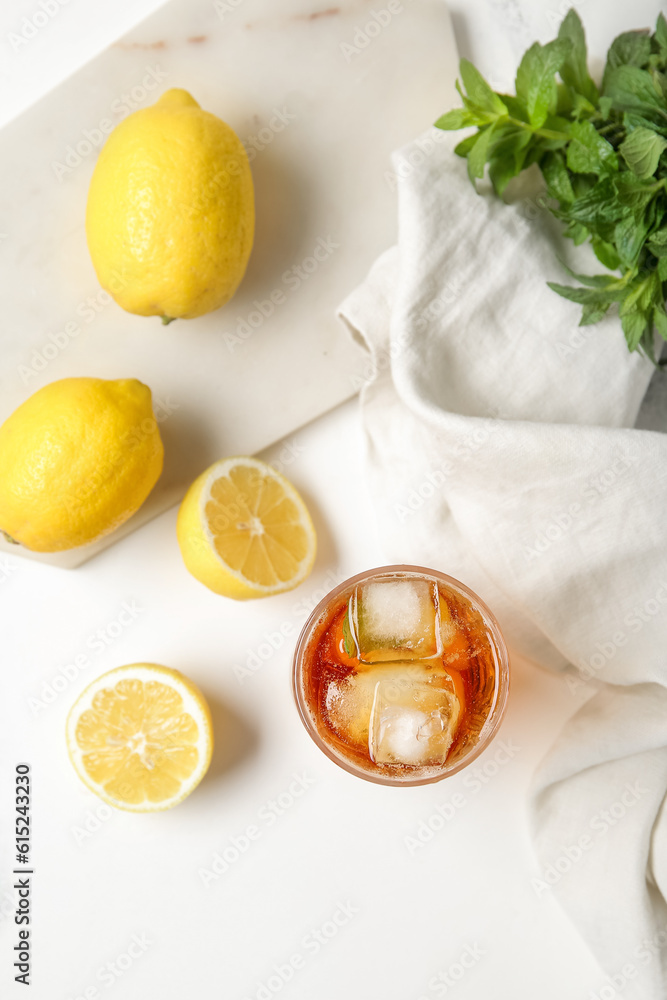 Glass of ice tea and board with lemons on white background