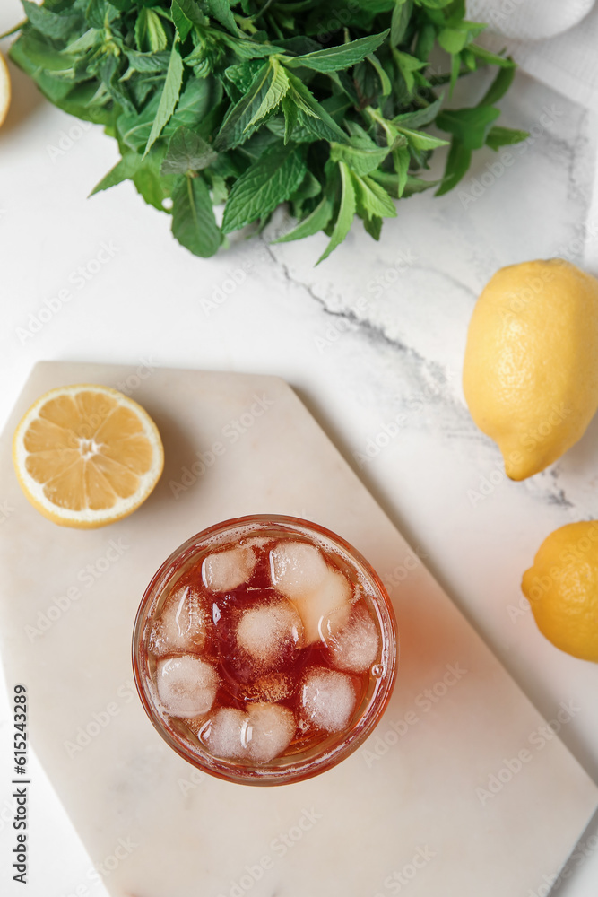 Board with glass of ice tea and lemons on white background