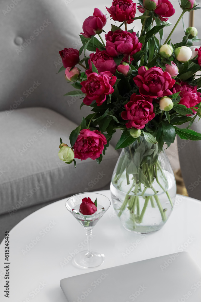 Vase with red peonies, glass and laptop on coffee table in living room