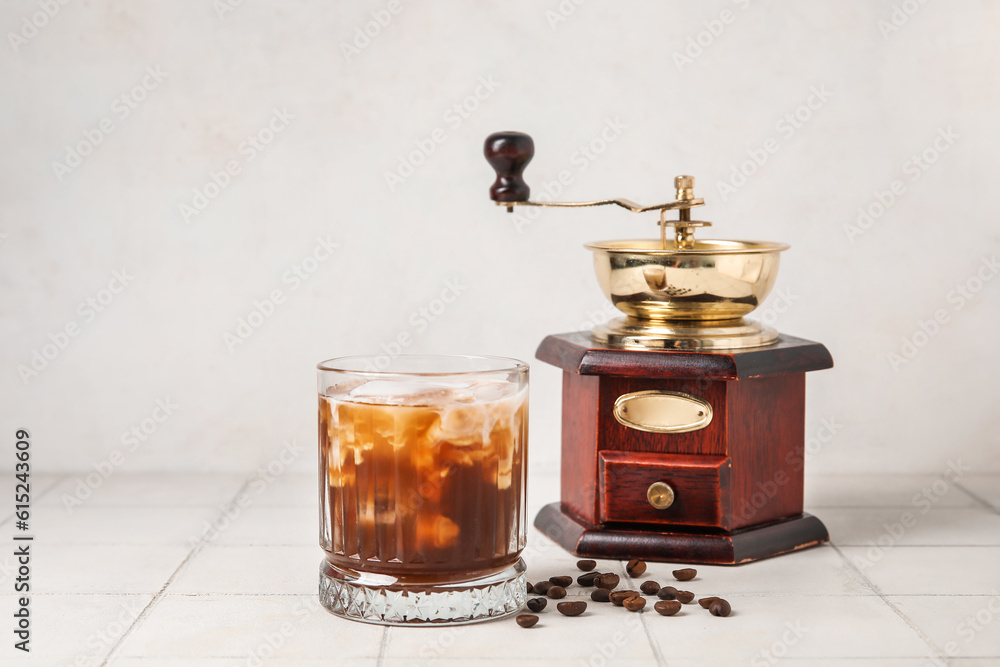 Glass of tasty ice coffee with milk and grinder on table