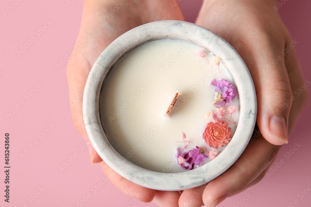 Female hands holding candle with flowers on pink background