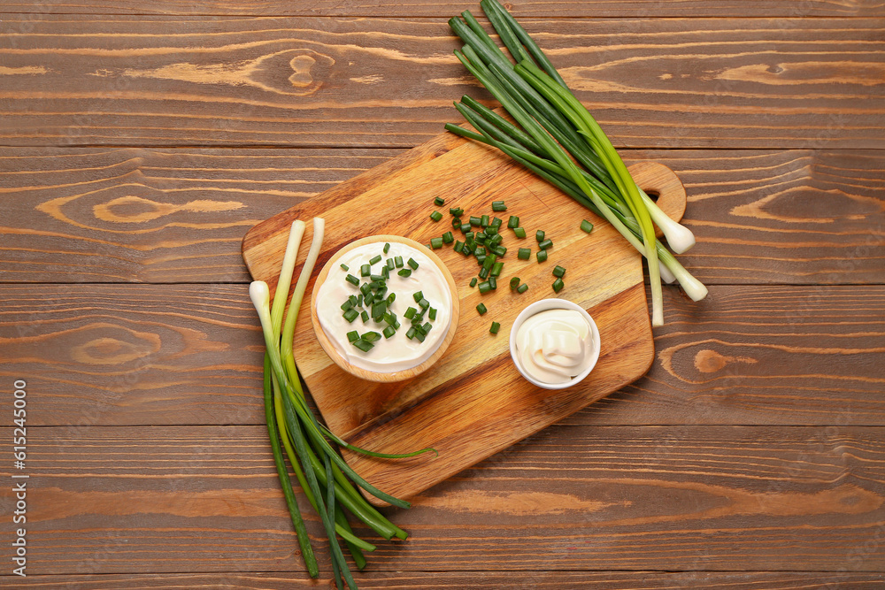 Bowls of tasty sour cream with sliced green onion on wooden background