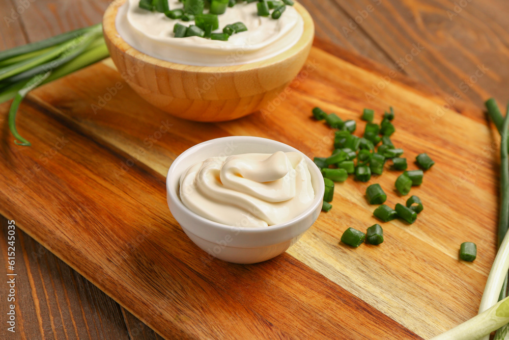 Bowls of tasty sour cream with sliced green onion on wooden background