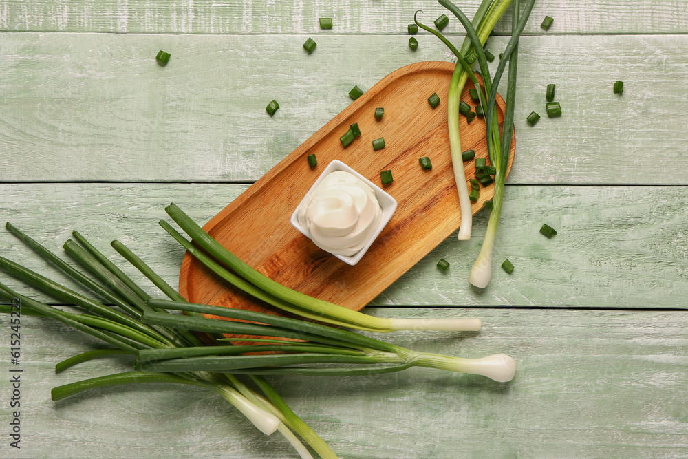 Board with bowl of tasty sour cream and scallion on green wooden background