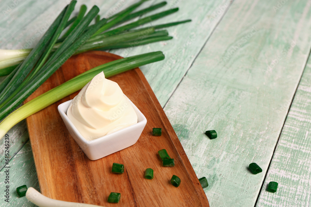 Board with bowl of tasty sour cream and scallion on green wooden background