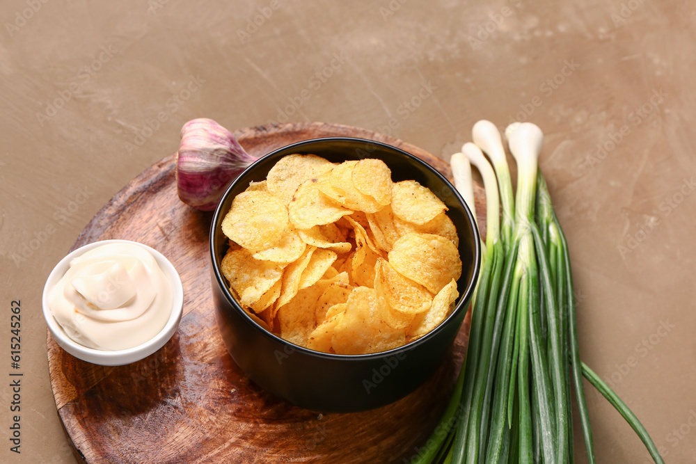 Bowl of tasty sour cream with green onion and potato chips on brown background