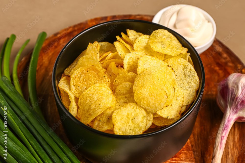 Bowl of tasty sour cream with green onion and potato chips on brown background