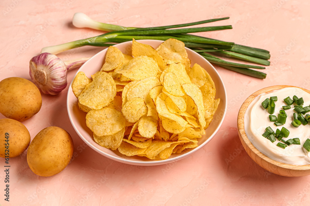 Bowl of tasty sour cream with sliced green onion and potato chips on pink background