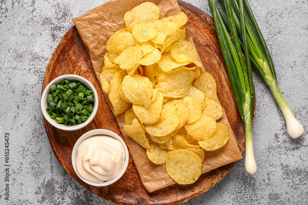 Bowls of tasty sour cream with sliced green onion and potato chips on grey background