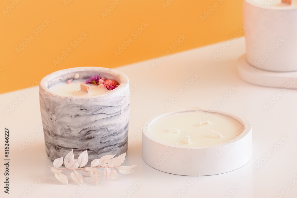 Holders with candles on table near orange wall in room, closeup