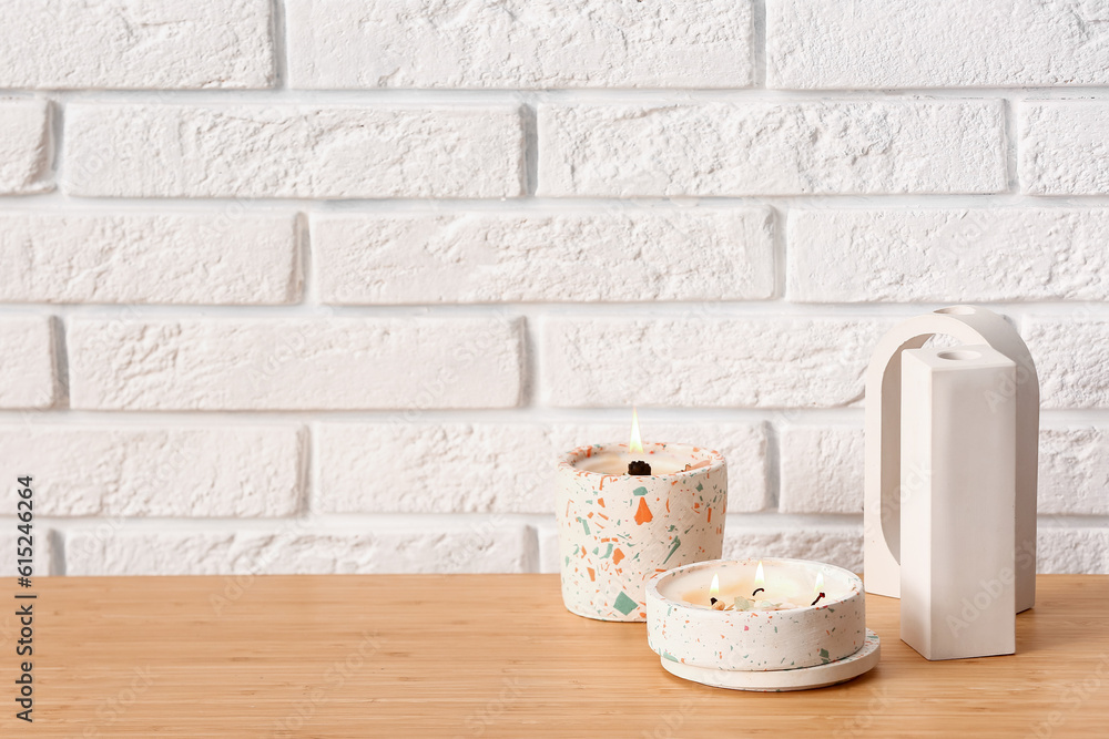 Holders with burning candles and decor on table near light brick wall in room