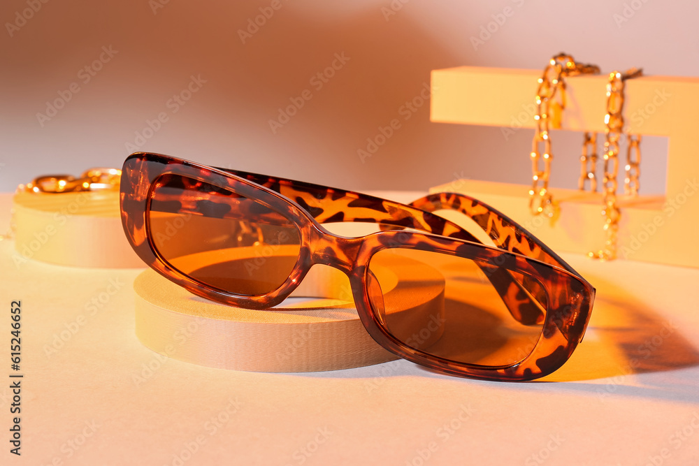 Podiums with stylish sunglasses and chain bracelets on orange background