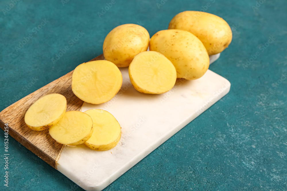 Board with raw baby potatoes on green background