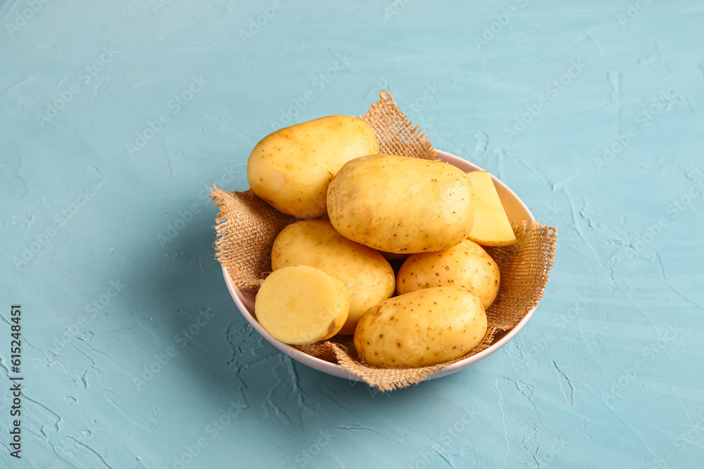 Bowl with raw baby potatoes on blue background