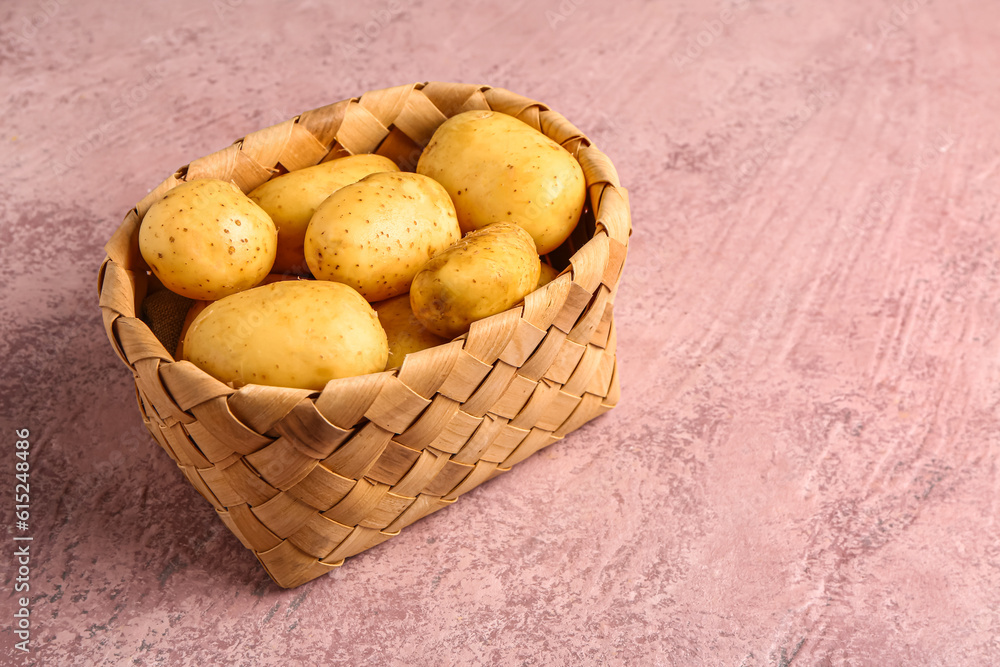 Wicker basket with raw baby potatoes on pink background