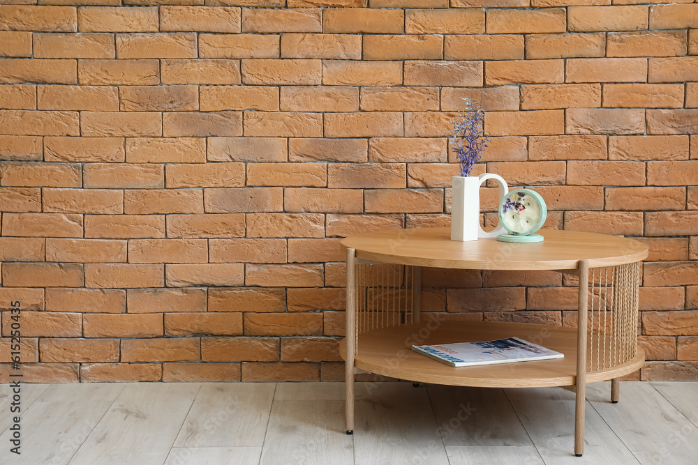 Beautiful branches and candle on table near brick wall in room