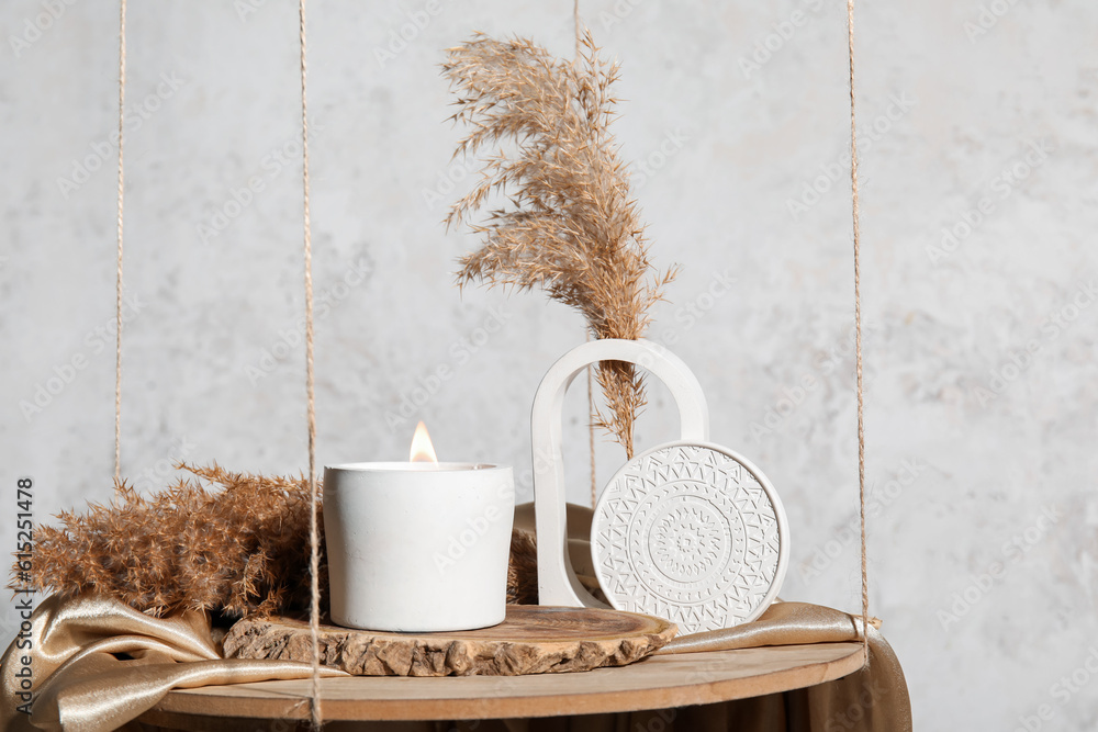 Holder with burning candle and pampas grass on hanging shelf near light wall in room, closeup