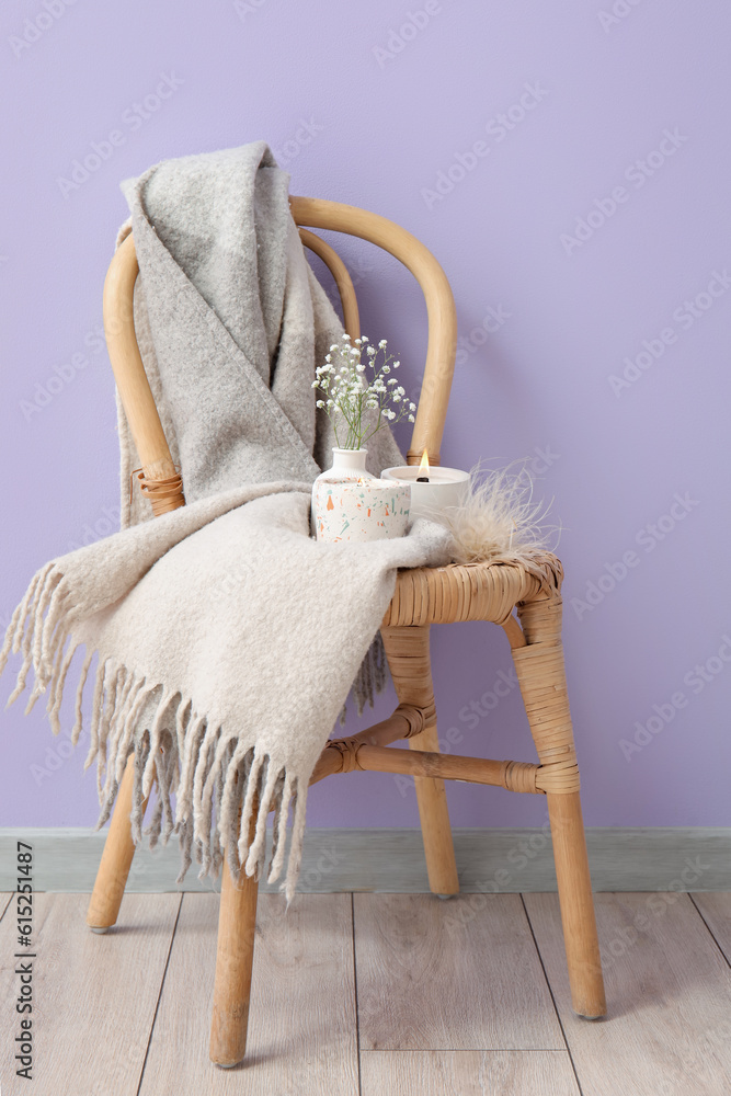 Holders with candles, gypsophila flowers and blanket on chair near purple wall in room